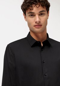 Camicia nera con colletto, texture liscia e maniche lunghe. Presenta bottoni neri e un design aderente.