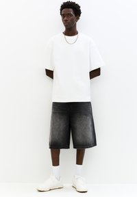 Hvid kortærmet t-shirt parret med mørkegrå denim shorts og hvide sneakers. Bemærkelsesværdig sølv kædeaccent. Enkel, afslappet design.