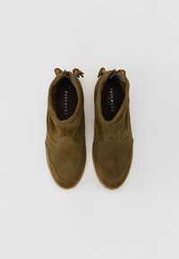 Bottes à chevilles en daim vert olive avec un design perforé, dotées d'une fermeture éclair sur le côté et d'accents de gland, à bout rond et avec une semelle texturée.