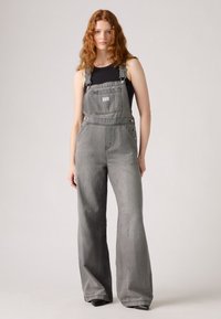 Gray denim overalls with wide legs, adjustable straps, front pocket, and side buttons. Paired with a black fitted tank top.