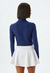 Top corto de manga larga en azul marino con un escote alto, combinado con una falda blanca acampanada. Texturas suaves y diseño ajustado.