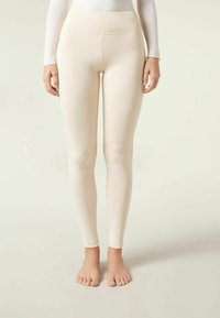 Leggings de color crema con cintura alta, que cuentan con una tela lisa y elástica y un diseño ajustado, que llegan hasta la mitad del tobillo.