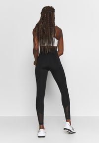 Zwarte high-waisted leggings met netpaneelaccenten en een aangesloten ontwerp, gecombineerd met een witte crop top en sportschoenen.