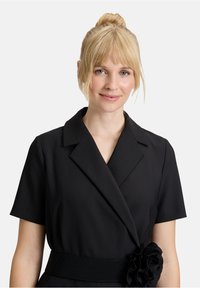 Czarna sukienka z krótkimi rękawami, dużym kołnierzem, teksturowanym paskiem i kwiatowym akcentem. Gładka tkanina z dopasowanym krojem.