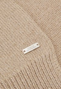 Tessuto a maglia beige con accenti metallici; include un'etichetta argento con la scritta "ARMANI EXCHANGE" in rilievo. Texture morbida, design a maglia larga.