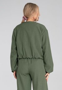 Oliwkowa, długosleeve'owa bluzka o luźnym kroju i elastycznym pasku w talii. Miękka, fakturowana tkanina; w zestawie ze spodniami w tym samym kolorze.