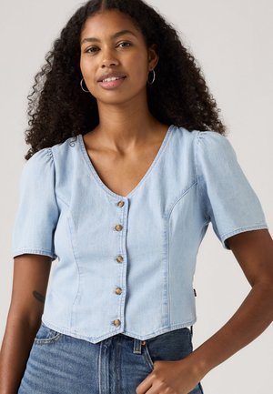 Lichtblauwe denim top met korte mouwen en een v-hals, versierde knopen en een getailleerde pasvorm. De stof heeft een zachte textuur en een lichte glans.