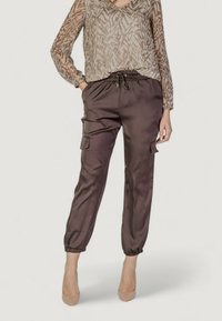 Pantaloni cargo in satin marrone con polsini elasticizzati, tasche laterali e vita regolabile con cordino, abbinati a un top con maniche lunghe a fantasia.