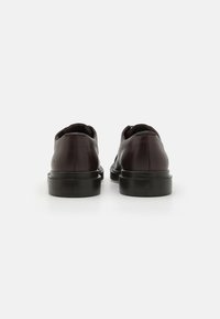 Scarpe in pelle marrone con finitura liscia, punta arrotondata e suola in gomma nera. Presentano un design minimale senza hardware o accenti visibili.