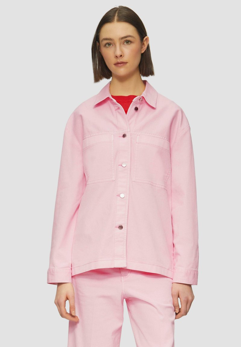 Roze denimjack met een knoopsluiting aan de voorkant, twee borstzakken en lange mouwen. Gecombineerd met bijpassende broek in dezelfde kleur. Zachte textuur.