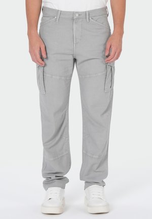 Man wearing light gray cargo pants with multiple pockets and white sneakers, standing against a plain white background.