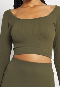 Top corto a coste verde oliva con maniche lunghe e scollatura ampia a forma di quadrato. Il tessuto presenta un motivo testurizzato e una vestibilità aderente.