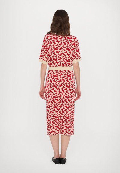 Rood en crèmekleurige jurk met vlinderprint, met korte mouwen, een nauwsluitende taille en een rok tot op de knieën. Zwarte instap-schoenen.