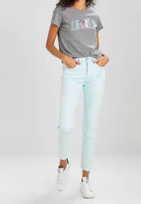 Camiseta de algodón gris con letras de estampado animal colorido, combinada con vaqueros de denim de color azul claro y zapatillas blancas. Ajuste y diseño casual.