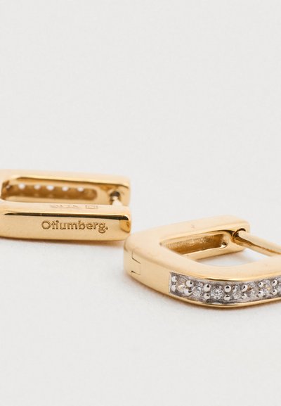 Χρυσά σκουλαρίκια με τετράγωνο σχήμα, που διαθέτουν μια σειρά από μικρές διαυγείς πέτρες κατά μήκος μιας πλευράς. Χαραγμένη σήμανση με το εμπορικό σήμα στη μία πλευρά. Ομαλή υφή.