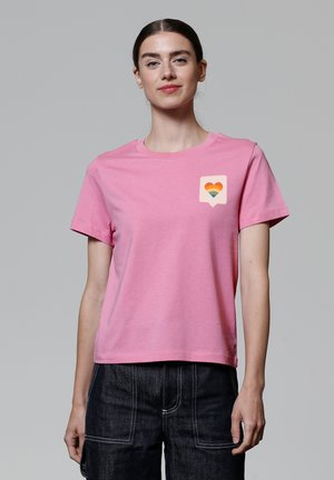 Roze katoenen t-shirt met een ronde hals, korte mouwen en een vierkante patch met een regenbooghart ontwerp op de linkerborst.