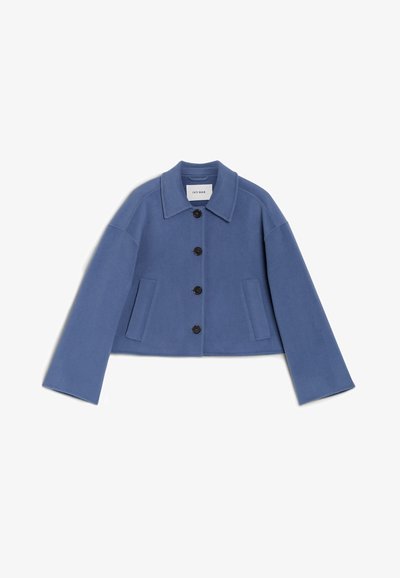 Przycięta, jasnoniebieska kurtka z gładkiego materiału. Ma rozłożysty kołnierz, zapięcie na guziki, dwie przednie kieszenie i szerokie rękawy.