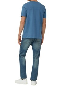 Hellblaues Baumwoll-T-Shirt mit Rundhalsausschnitt, kombiniert mit ausgewaschenen blauen Jeans. Das Model trägt weiße Sneakers. Ansicht von hinten zeigt die Länge und Passform des Shirts.