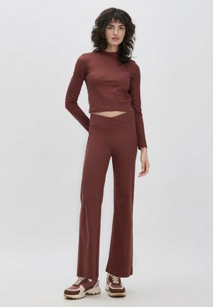 Ribbed, bordeauxfarbener Langarm-Crop-Top, kombiniert mit passenden, figurbetonten Flared Pants. Das Modell trägt klobige Sneaker, die den lässigen Sitz und die Textur betonen.
