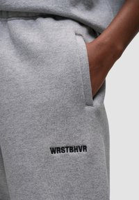 Grijze sweats met een zachte textuur, elastische tailleband en zijzakken. Zwart geborduurde tekst "WRSTBHVR" op de linker dij.