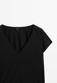 Chemise noire à manches courtes avec un col en V et une couture centrale visible sur fond blanc.