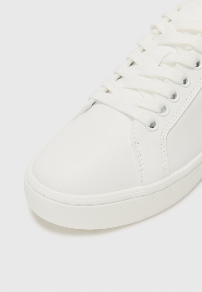 Białe skórzane sneakersy z gładkim wykończeniem, okrągłym noskiem, sznurowanym zapięciem i gumową podeszwą z detalami szycia po bokach.