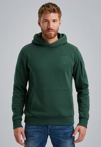 Green hoodie made of cotton-blend material, featuring a kangaroo pocket, ribbed cuffs, and a patch logo on the chest. Casual design.