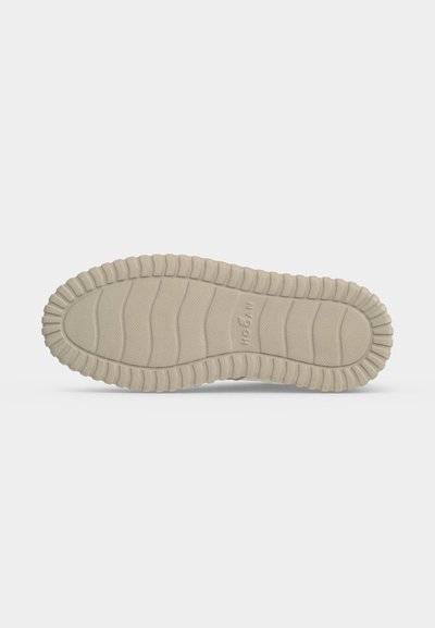 Semelle de chaussure beige avec motif texturé antidérapant et lignes de bande de roulement courbes, présentée à plat sur fond blanc.