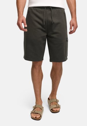 Uomo che indossa pantaloncini grigio scuro fino al ginocchio con coulisse e tasche con cerniera, abbinati a sandali beige con doppio cinturino, in piedi su sfondo bianco.