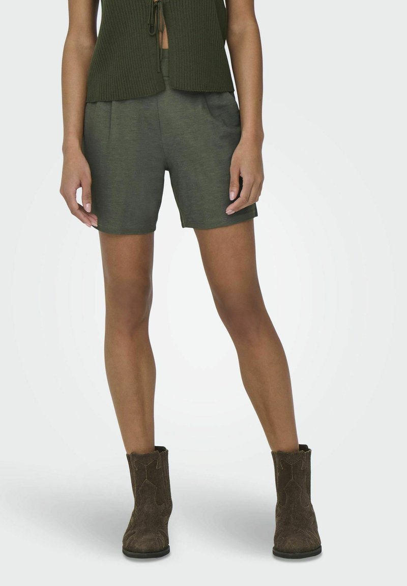 Olivengroene shorts met een gladde textuur, voorzien van een platte voorkant en zijzakken. Gecombineerd met bruine, gestructureerde enkellaarzen.