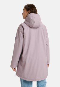 Chaqueta impermeable de color púrpura claro con capucha, con un corte relajado y un diseño minimalista. Textura lisa y sin patrones visibles.