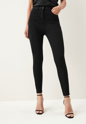 Černé skinny džíny s vysokým pasem vyrobené z elastického materiálu, s knoflíkovým zapínáním, poutky na pásek a kapsami, doplněné černými páskovými podpatky.