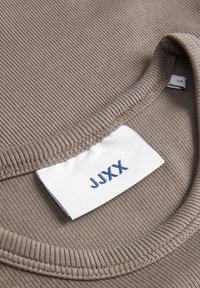 Brązowa t-shirt z prążkowanego materiału z okrągłym dekoltem. Zawiera metkę z napisem "JJXX" nadrukowanym na niebiesko oraz metkę rozmiaru umieszczoną z boku.