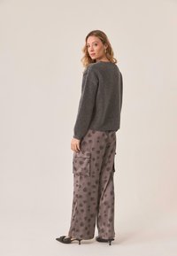 Suéter de punto gris de manga larga combinado con pantalones anchos de estampado con diseño de hojas. Modelo de espaldas, zapatos negros.