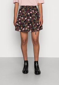 Jupe noire à fleurs avec un design évasé, ornée de fleurs roses et jaunes, associée à des bottines noires brillantes avec un détail de fermeture éclair argentée.