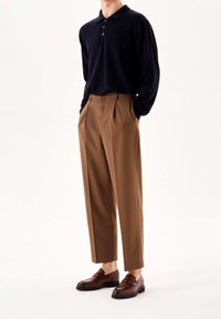Polo à manches longues bleu marine, pantalons plissés beiges et mocassins marron. La tenue présente une coupe classique avec des textures lisses et un design simple.