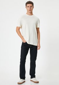 Camiseta de algodón blanca de mangas cortas, combinada con jeans de color azul oscuro. Las zapatillas tienen parte superior blanca con suelas de goma marrón.