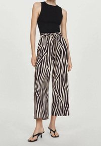 Haut noir sans manches associé à un pantalon beige à jambes larges avec un motif audacieux de rayures zébrées noires et un détail de taille nouée.