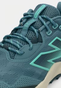 Türkiissinine spordijalats võrgust pealiskihiga, tekstuursete detailide ja silmapaistva logoga. Paelte süsteem kontrastsete roheliste esiletõstmistega.