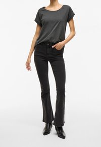 Mørkegrå t-shirt med rullede ærmer, kombineret med sorte flare jeans. Modellen bærer sorte ankelstøvler. Minimalistisk design, glat stof.