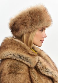 Cappello di pelliccia marrone con la parte superiore arrotondata e il bordo svasato, abbinato a un cappotto di pelliccia marrone coordinato, caratterizzato da un colletto spesso e una texture morbida.