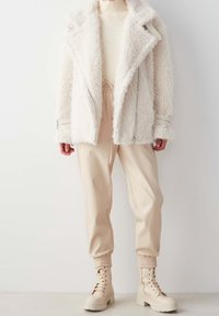 Cazadora de borrego blanca y difusa con un diseño de doble botonadura, pantalones ajustados beige y botas de combate de color claro con suela gruesa.