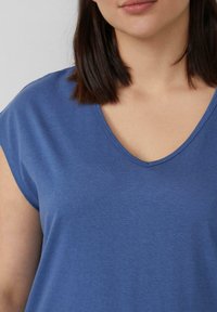 Niebieska koszulka krótkim rękawem z dekoltem w serek, wykonana z miękkiej tkaniny. Charakteryzuje się gładką fakturą i luźnym krojem.