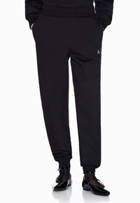 Zwarte sweatpants van zacht materiaal, met zijzakken, een elastische tailleband en aansluitende boorden, gecombineerd met glanzende zwarte schoenen.