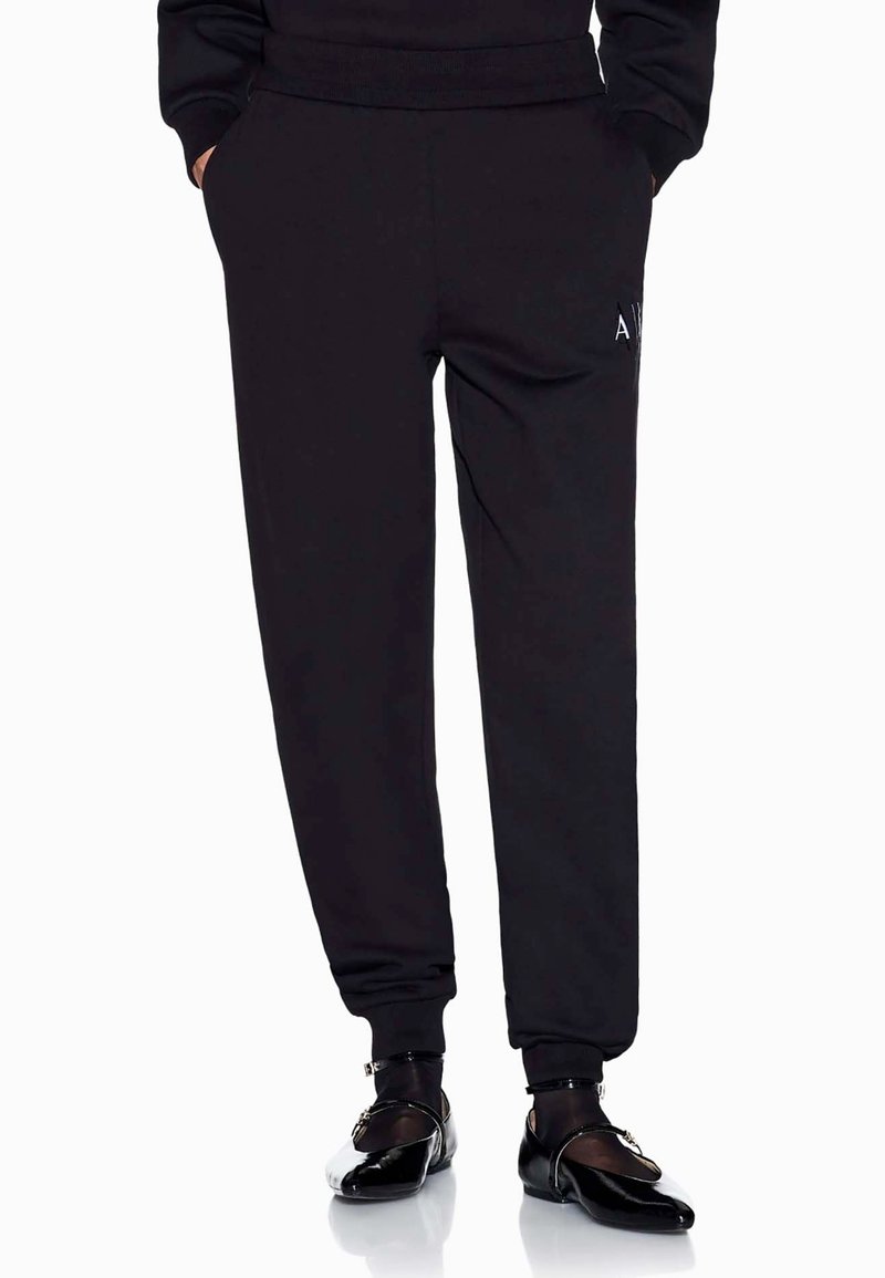 Zwarte sweatpants van zacht materiaal, met zijzakken, een elastische tailleband en aansluitende boorden, gecombineerd met glanzende zwarte schoenen.