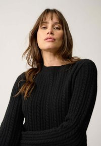 Czarny sweter prążkowany z okrągłym dekoltem i długimi rękawami, wykonany z miękkiego materiału dzianinowego z widocznymi wzorami tekstury.