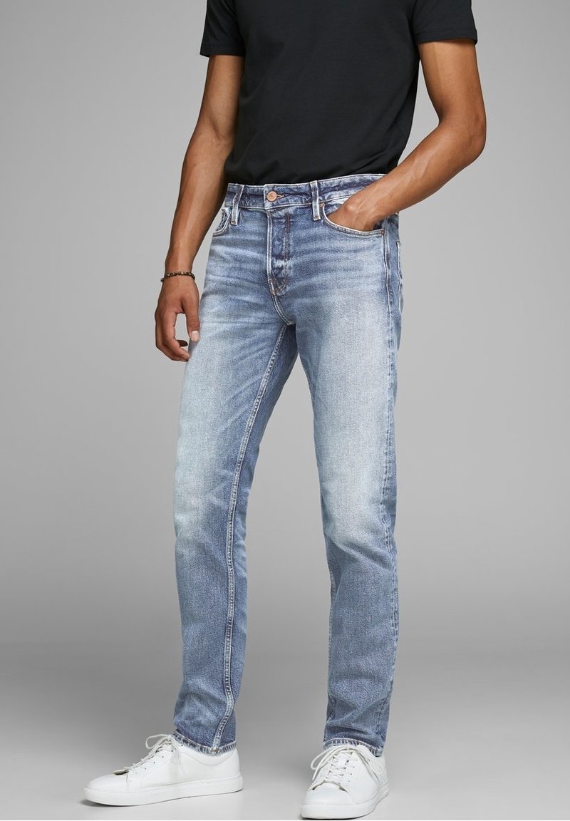 Ljusblå denimjeans med rak passform, blekt utseende och lätt slitage. I kombination med vita sneakers och en svart t-shirt.