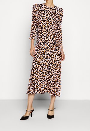 Kvinde iført en midilang leopardprint kjole med lange ærmer og sorte spidse høje hæle med ankelremme.
