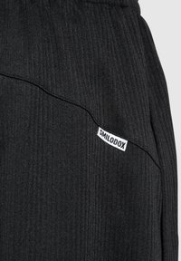 Schwarze, gerippte Jogginghosen mit einem elastischen Bund, ausgestattet mit einem weißen "SMILODOX"-Label an der Seite. Die Textur ist weich und weist feine vertikale Linien auf.