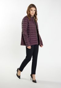 Jachetă puffer burgundă cu un design matlasat, guler înalt și fermoar auriu; asortată cu pantaloni negri mulați și tocuri negre.